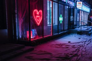 Neonreklame mit einem roten Herz in einem Bordell neben einem neongrünen Kreuz einer Apotheke in einer dunklen, verschneiten Straße Moskaus.
